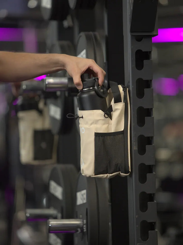 Hand lifting a bottle out of the beige RYVO Rig magnetic gym bag on a gym rack