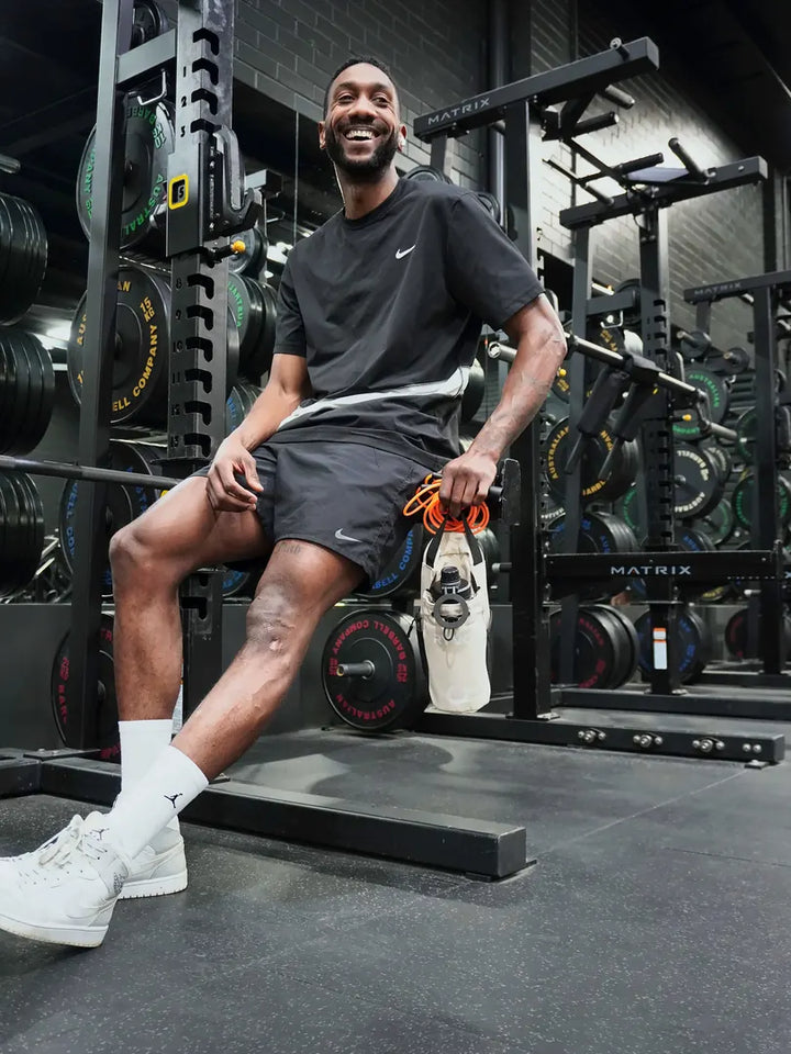 Smiling man sitting on a gym rack holding the beige RYVO Rig gym bag